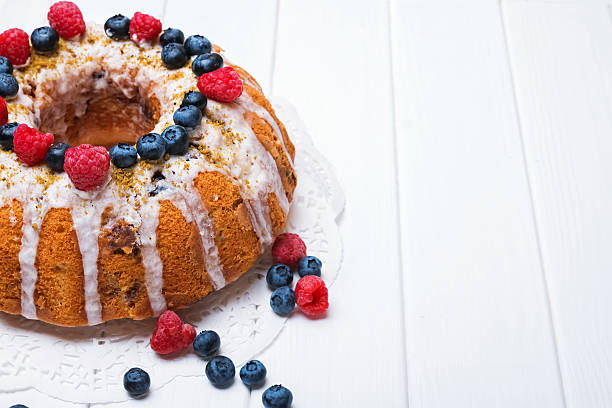 Delicious bundt cake with berries on white wooden table close-up
