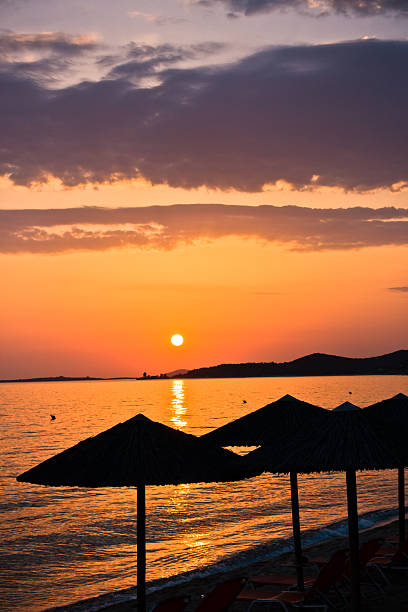 Sandy beach with stray sunshades and orange chairs at sunset in Sithonia, Greece