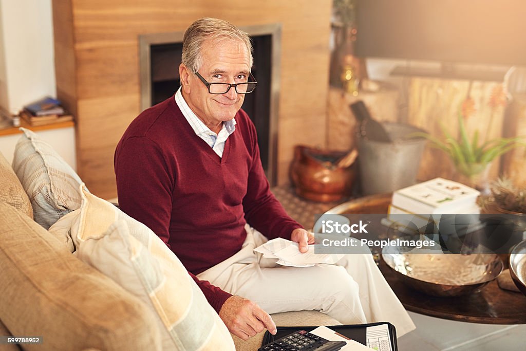 Saving money and stretching dollars is important Shot of a senior man working out a budget while sitting on the living room sofa 70-79 Years Stock Photo