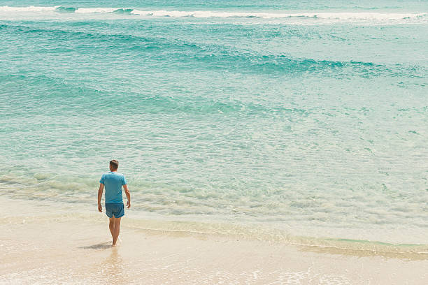 middle aged man paddling along the waters edge on a idyllic calm June morning at Pedn Vounder Beach, South Cornwall.