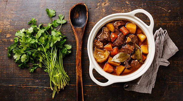Beef meat stewed with potatoes Beef meat stewed with potatoes, carrots and spices in ceramic pot on wooden background beef stew stock pictures, royalty-free photos & images