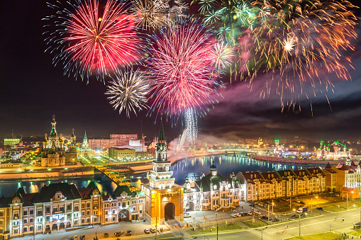 Festive view of the city with night illuminations. Beautiful brick buildings, churches and towers in the city's center. Fireworks over city on City holiday. Volga region of Russia, the city of Yoshkar-Ola