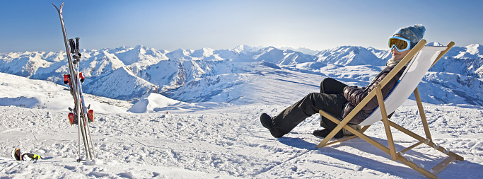 Panorama of a girl sunbathing in a deckchair near a snowy ski slope