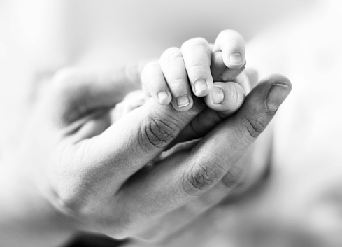 Baby holding the mothers hand, trust theme. Black and white toned image with holding hands of a newborn baby and it's parent.