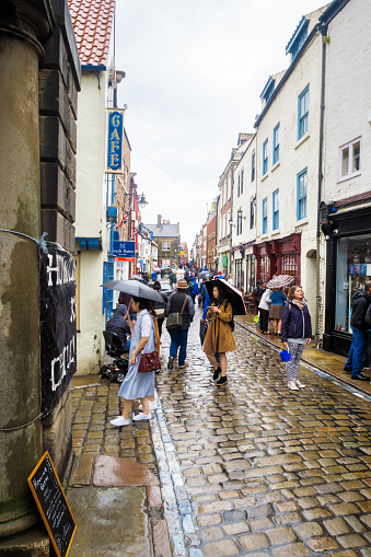 Whitby, England - September 3, 2016: Group of oriental tourists and various other people on Church Street, on a very rainy day. In Whitby, North Yorkshire, England. On 3rd September 2016.