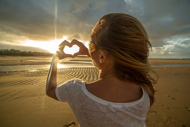istock Caucasian female on beach makes heart shape finger frame 599876526