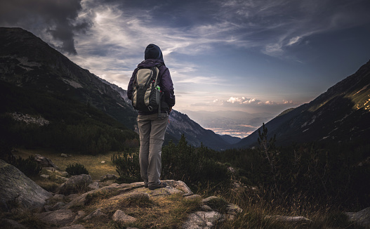 Traveler with large backpack watching the sunset over the mountains. Stock photo.