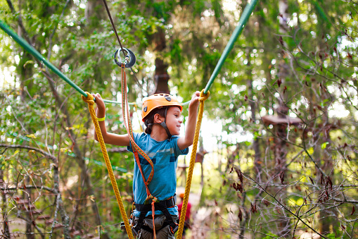 cheerful child bravely overcomes extreme rope route outdoors. ziplining