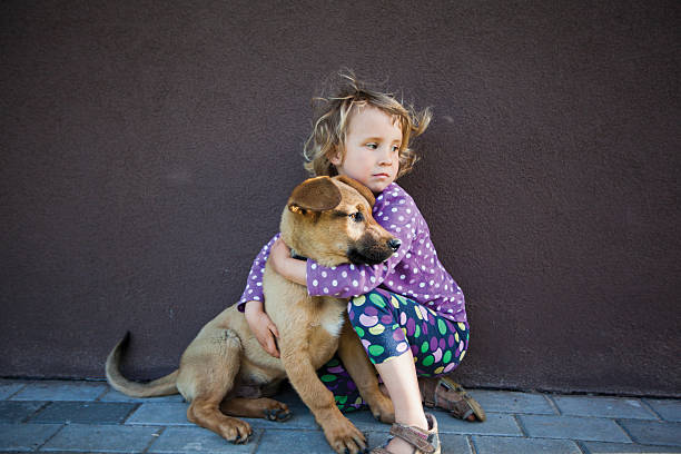 Little girl giving hugs to her puppy, looking in the same direction, wind in her hair. Concept love and care.