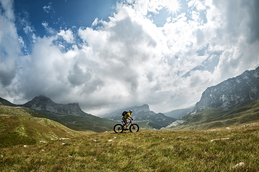 Male cyclist riding his fat bike while exploring new off-road areas and beautiful panoramic nature in the mountains. Mountain peaks are in the background.