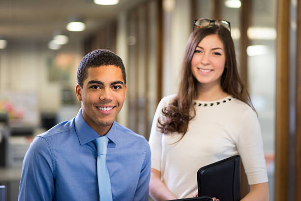 university students on a work placement . young man and woman stand in their new workplace smiling proudly to camera . businesswear stock pictures, royalty-free photos & images