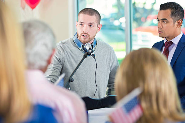 istock Man giving speech at podium during town hall meeting 599893814