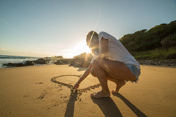 istock Female drawing heart on sand 599900056