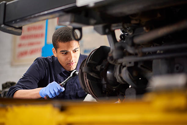 Mechanic repairs A young mechanic is working on a car in a garage repair shop. He is wearing blue overalls.  He is fixing the brake discs on the front driver's side of the vehicle. brake disc photos stock pictures, royalty-free photos & images