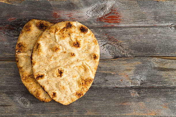 Simply delicious baked naan flatbreads on Picnic Table Simply delicious baked crusty whole grain naan flatbreads, a leavened bread cooked in a tandoor clay oven, served on authentic old wooden Picnic Table shot from above with copyspace on the right flatbread photos stock pictures, royalty-free photos & images