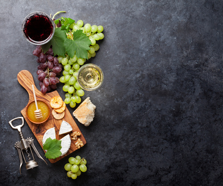 Red and white wine glasses, grape, cheese and honey over stone table. Top view with copy space