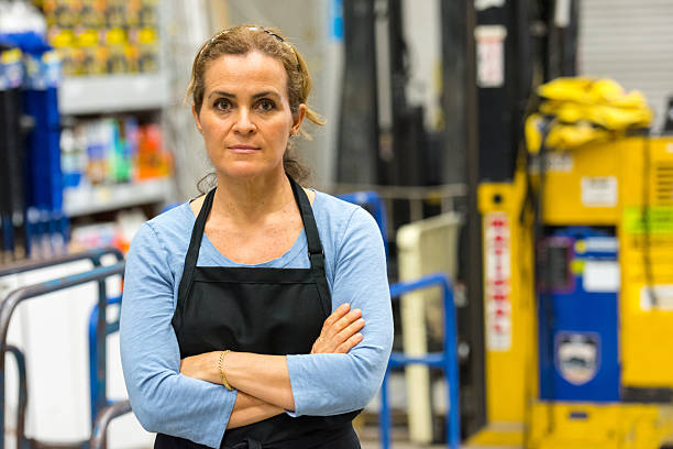 Working in a hardware store warehouse mature woman Working in a timber/lumber hardware store warehouse looking at the camera with her arms crossed menial job stock pictures, royalty-free photos & images