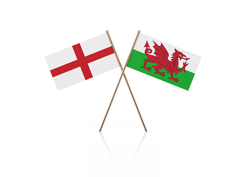 Tiny English and Welsh flag pair on gold sticks. Flag pair is standing on a reflective surface. Isolated on white background. With clipping path.