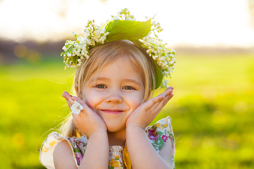 Cute little girl with blond hair in a wreath of lily of the valley in the spring garden