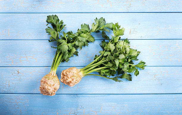 Organic celery Two roots of organic celery with green leaves on blue wood background Celeriac stock pictures, royalty-free photos & images