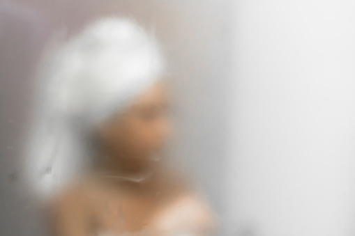 Young woman reflected in the mirror blurred by the steam. Defocused blurry background.