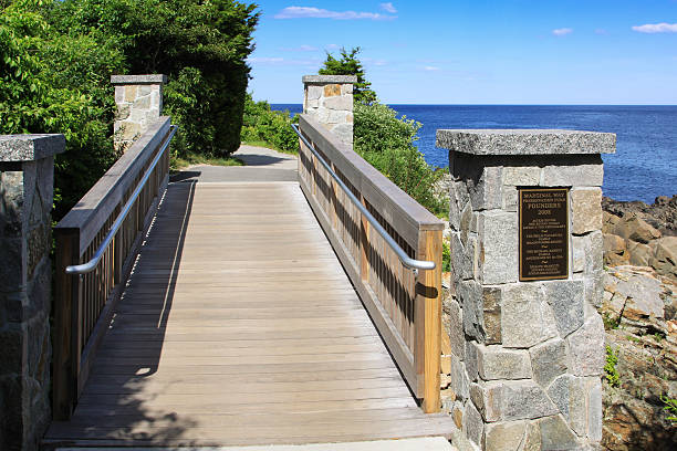 Ogunquit, ME, USA - June 30, 2010: Footbridge at Marginal Way, Rocks and Ocean in Ogunquit, Maine, New England, USA. Blue ocean waters, rocks and green bushes are in the image. Canon EF 24-105mm f/4 L IS lens. Polarizing filter.