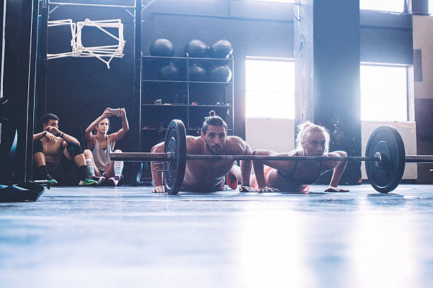 Cross training Young athletes exercising in gym. Doing burpees over bar.  Friends filming them with smartphones. Professional athletes. Wearing sports clothing. burpee stock pictures, royalty-free photos & images