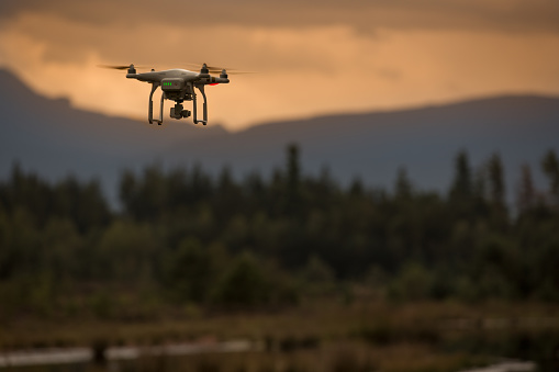 Schönram, Germany - September 5, 2016: Drone in flight at sunset. Battery lights indicate full main battery, as the quadrocopter hovers above the tiny lake in the moor. 