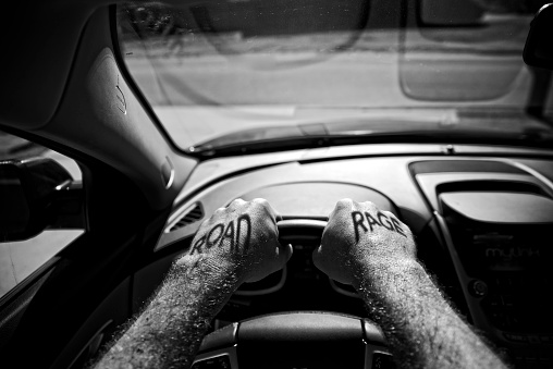 hands grip a car's steering wheel with the shadow letters Road Rge projected onto each hand.
