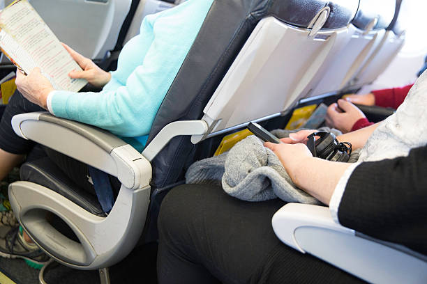 Passengers seated on an airplane are cramped in their seats In this real situation a row of unidentifiable passengers are sitting in their seats on an airplane. The seating is tight. Their legs are touching the seats in front of them. vehicle seat stock pictures, royalty-free photos & images