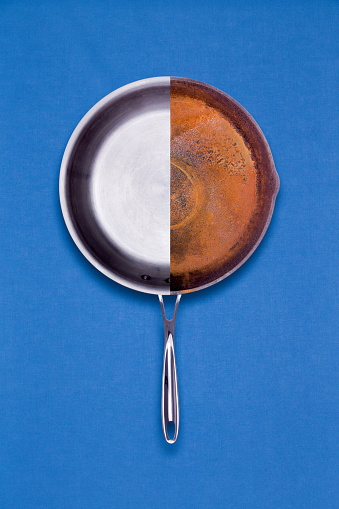 New teflon coated non-stick and old rusted frying pan combined into one halved unit for comparison of age and condition in a conceptual overhead view on a blue background