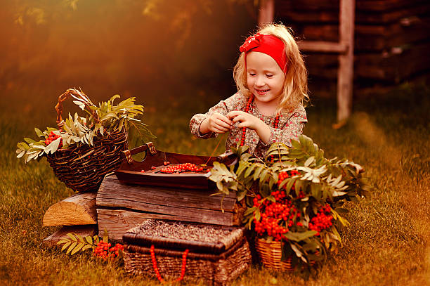 mignon fille en bas âge faire des perles de baies dans le jardin d’automne - autumn table setting flower photos et images de collection