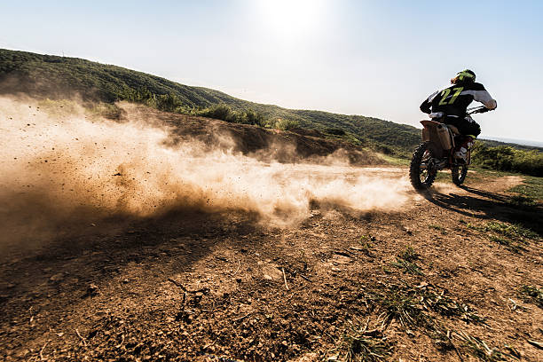 vista posteriore del pilota di motocross che guida velocemente su strada sterrata. - scrambling foto e immagini stock