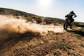 Back view of motocross rider driving fast on dirt track.