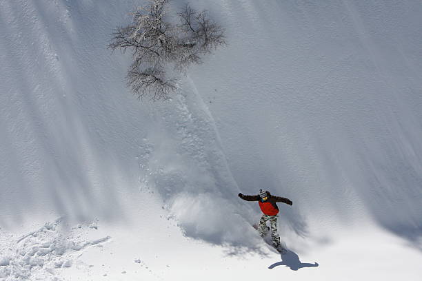 snowboarding down the snowy mountain terrain at the ski resort - ski jumping snowboarding snowboard jumping imagens e fotografias de stock