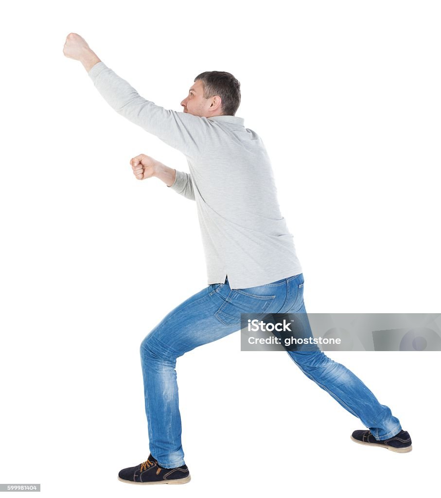 back view of standing man pulling a rope from the back view of standing man pulling a rope from the top or cling to something. guy watching. Rear view people collection.  backside view of person.  Isolated over white background. resting his foot guy pulls something from above Pulling Stock Photo