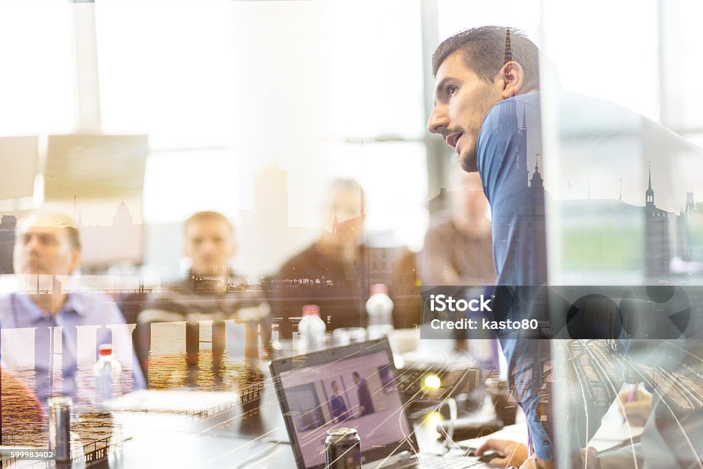 Business presentation on corporate meeting. Business man making a presentation at office. Business executive delivering a presentation to his colleagues during meeting, explaining business plans to his employees. City reflection in window. Business Stock Photo