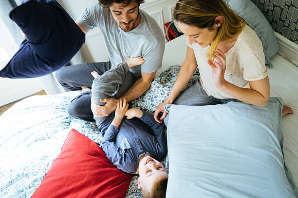 feliz familia despertar por la mañana, jugando en la cama - bed couple pillow fight men fotografías e imágenes de stock