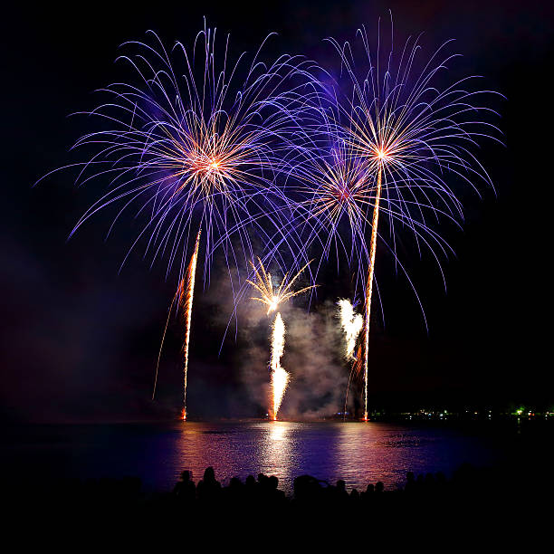 istock Beautiful blue colorful fireworks display with unrecognizable crowd people watching 599994558