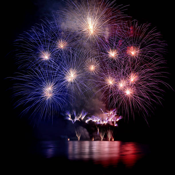 Beautiful blue white and red large fireworks with water reflections Square composition color photography at night of beautiful large colorful fireworks display with awe pyrotechnic effects at edge of the water with some abstract reflections in water wave. This fireworks is blue, white and red colored like colors of French flag or American flag. Taken during celebration event like new year or national day. The original picture was taken during the Bastille Day in France, 14th of July, along Rhone river in Isere department in Auvergne-Rhone-Alpes region in Europe in Montalieu-Vercieu city. bastille day photos stock pictures, royalty-free photos & images