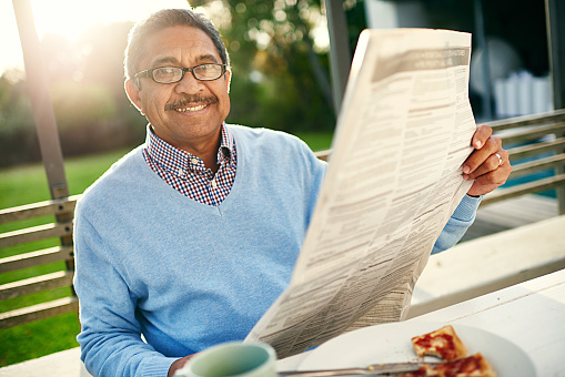 Portrait of a happy older man reading a newspaper with his breakfast outdoors