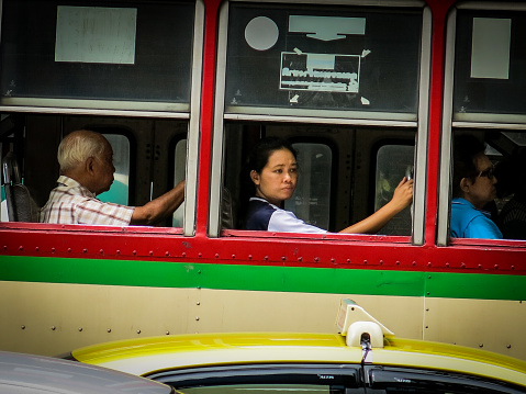 Bangkok, Thailand - June 5, 2016: A close up image of real people in authentic daily life in Bangkok, Thailand.  The Summer months in the city are stifling and the public transport windows always open, due to having no air con.  One woman stares out into the bustling street, she looks far away in her thoughts.