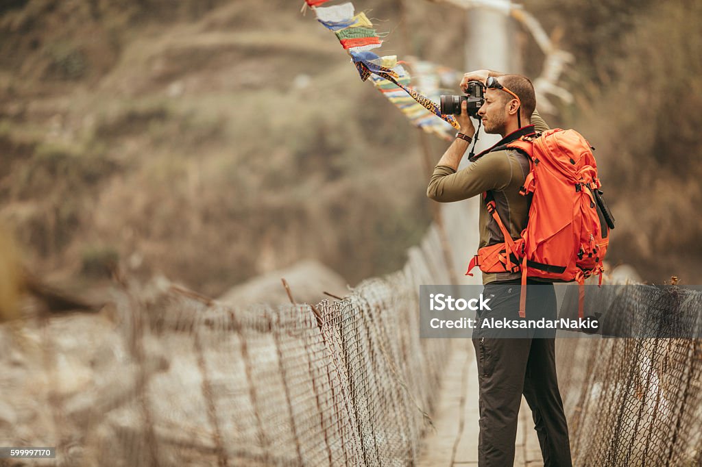 Hiker capturing the view Photo of a hiker capturing the view over the bridge in Annapurna Range on Himalayas, Nepal Travel Stock Photo