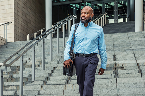 Photo of a mid adult African American businessman walking down a set of steps with his laptop back slung over his shoulder