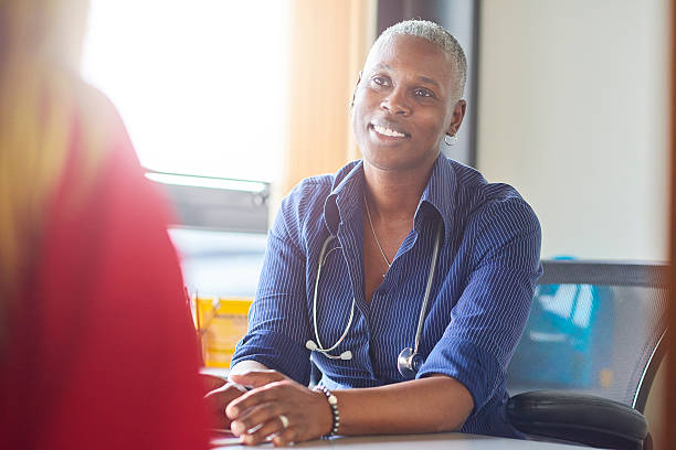 Doctor gives the all clear A female doctor sits at her desk and chats to a female patient.  She is a blue shirt with the sleeves rolled up and a stethoscope around her neck. rolled up sleeves stock pictures, royalty-free photos & images