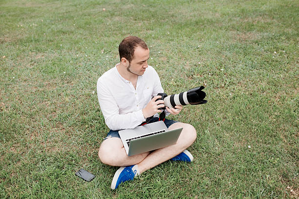 istock Young man photographer using laptop and camera in the park 600056480