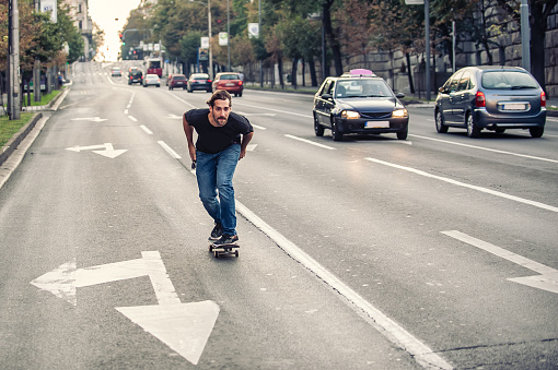 Professional skateboarder riding a skateboard slope on the capital city streets, through cars and urban traffic