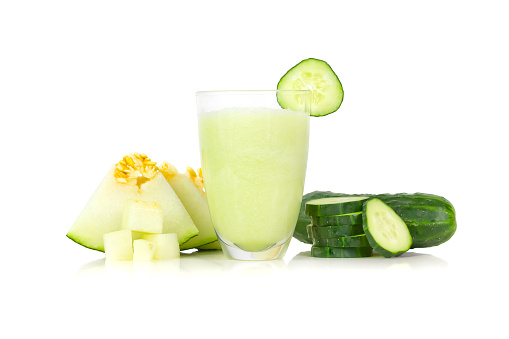 A glass in the center of the image surrounded by pieces of cucumber and melon, over a white background.