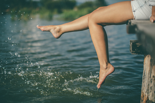 Young woman splashing water with beautiful legs at lake