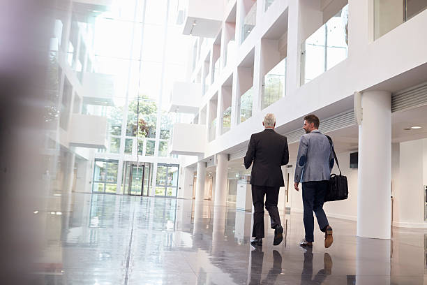 Rear View Of Businessmen Walking Through Office Lobby